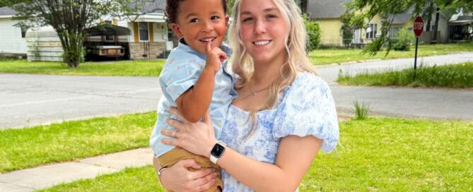 Karmen holds her toddler son outside in the grass.