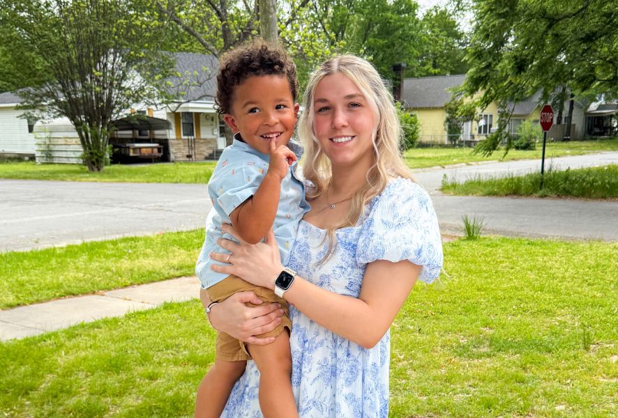 Karmen holds her toddler son outside in the grass.