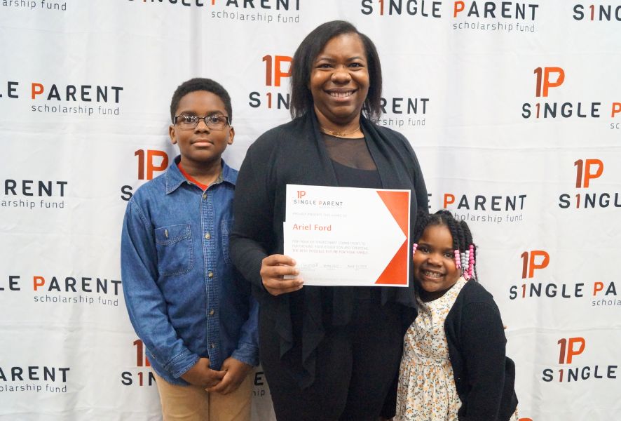 Ariel Ford holds her single parent scholarship with her two children. They stand in front of an ASPSF banner.