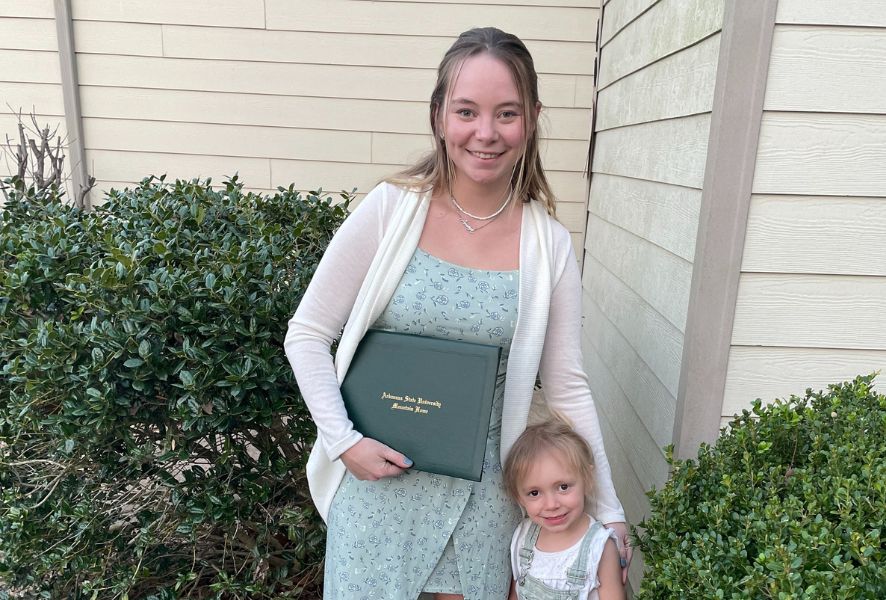 Mom Danielle Frencl holds her degree in one hand and her toddler daughter in another.
