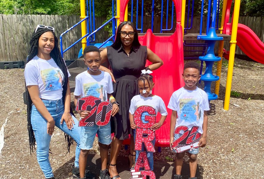 Kimberly Broadway and her four kids stand in a playground. The kids are holding signs that say "2024 Grad."