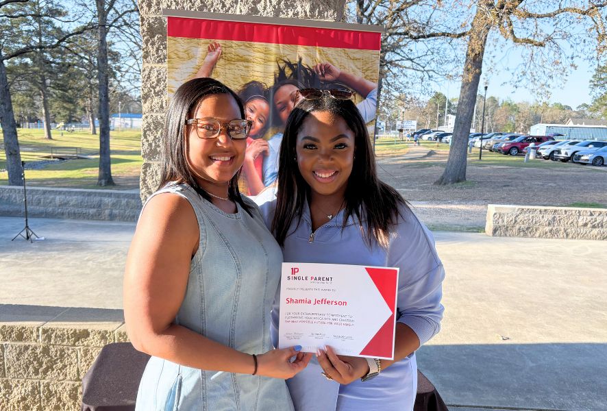 Two women hold up a scholarhsip certificate outside.