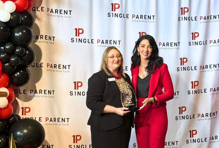 Jenn Morehead and Bailey Hutcheson hold an award in front of an ASPSF step and repeat