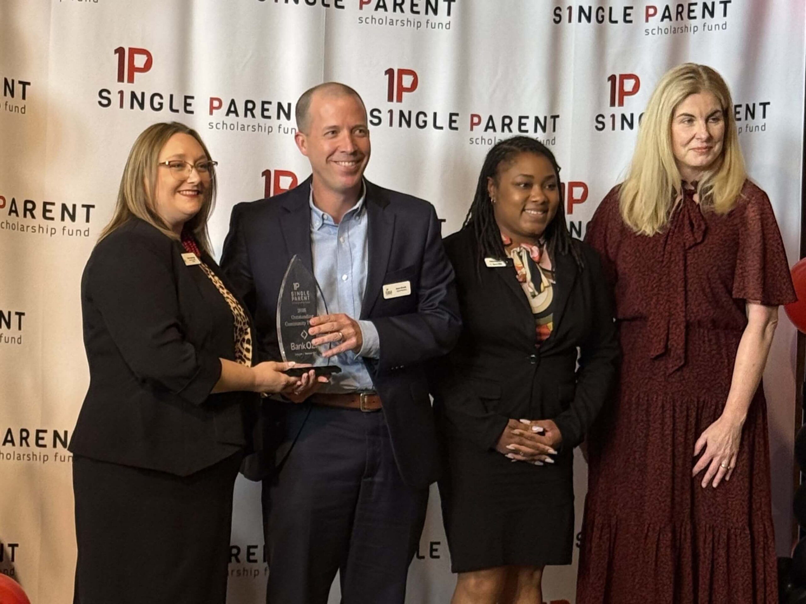 Bank OZK-Outstanding Community Partner Jenn Morehead and Members from Bank Ozk stand in front of step-and-repeat with an award.