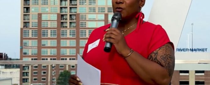 Kristy holds a microphone against a Little Rock skyline background