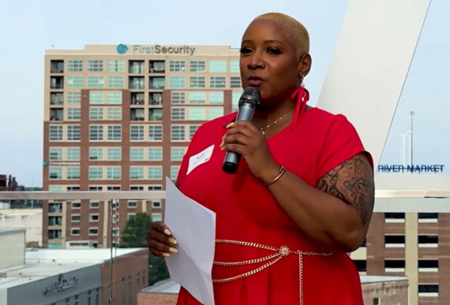 Kristy holds a microphone against a Little Rock skyline background